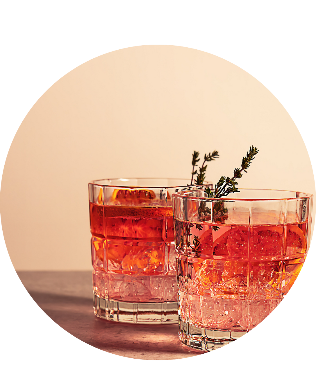 Two colorful cocktails on a wooden table, garnished with fruit and herbs.